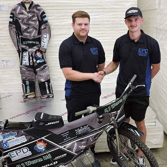 Two men shaking hands beside racing motorcycle and gear.
