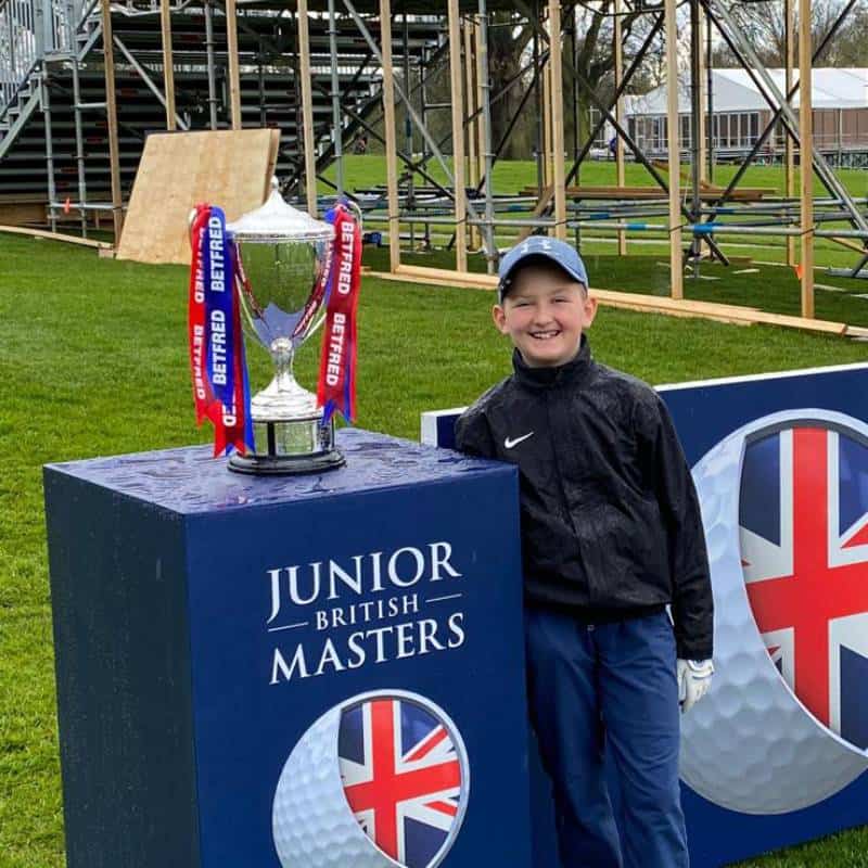 Boy smiling by Junior British Masters golf trophy.