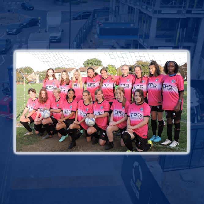 Women's football team posing in pink jerseys on field.