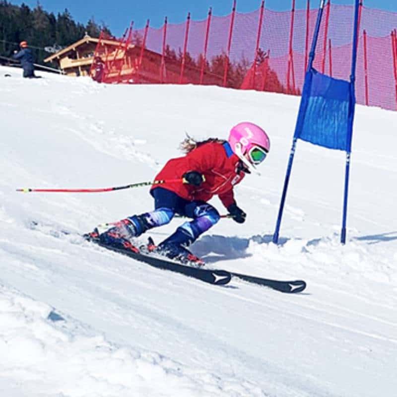 Child in pink helmet skiing slalom on snowy slope.