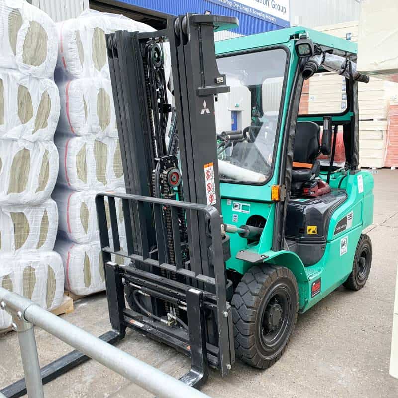 Green forklift carrying insulation rolls at warehouse.