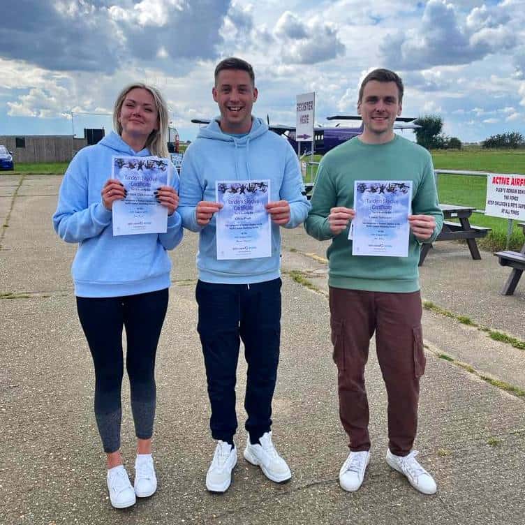Three friends displaying certificates at airfield.