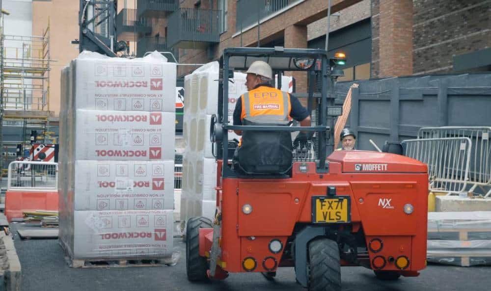 Forklift operator moving insulation materials at construction site.