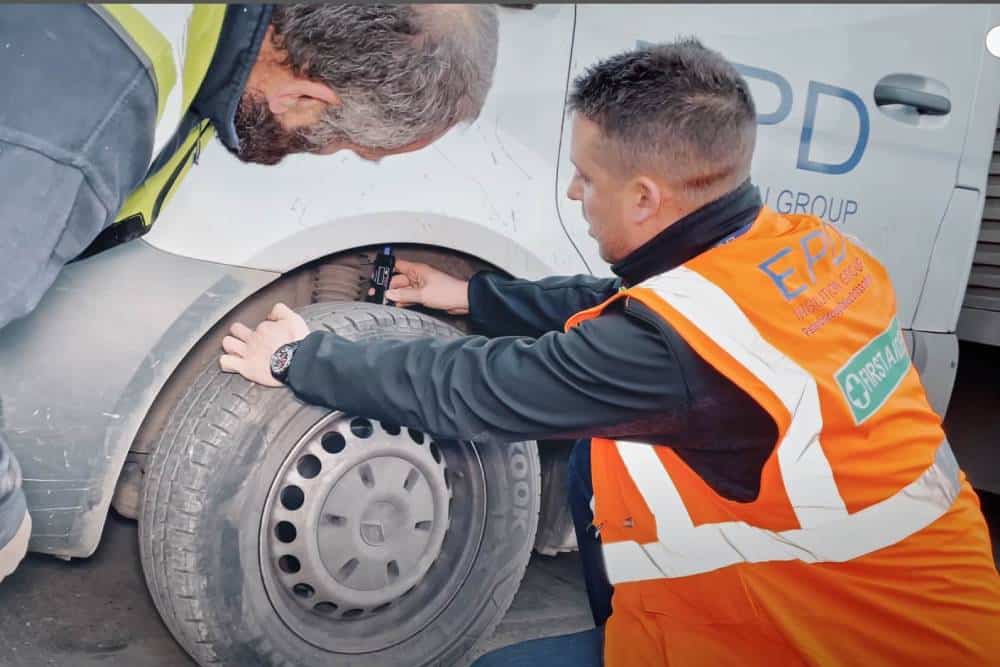 Two men inspecting a car tyre roadside.