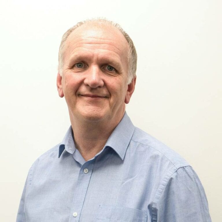 Middle-aged man smiling in blue shirt against white background.