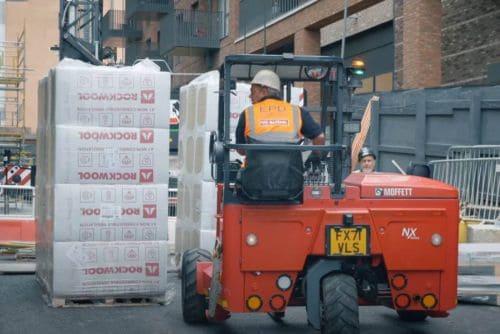 Worker operating forklift to move stacked goods on street.