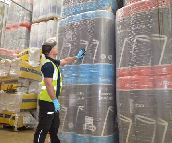 Worker inspecting large rolls of industrial insulation material.