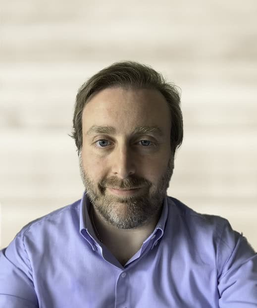 Man in purple shirt with beard and wooden background.