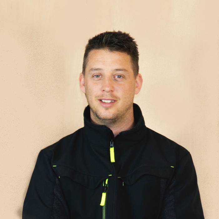 Man in black jacket smiling, beige background.