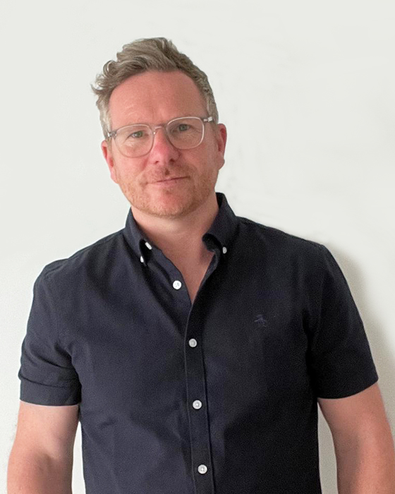 Man in dark blue shirt standing against white wall