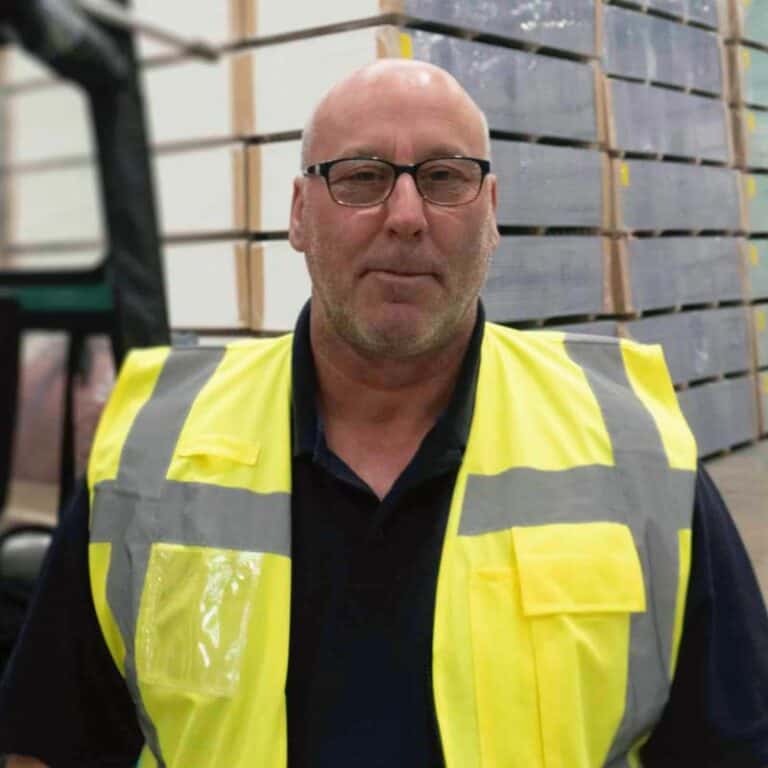 Bald man in high-visibility jacket in warehouse.