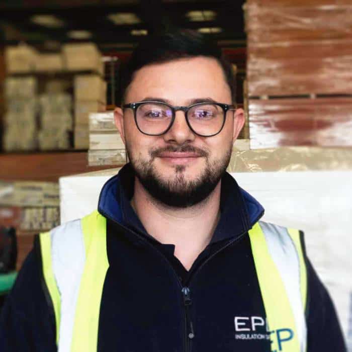 Smiling man in warehouse wearing glasses and hi-vis vest.