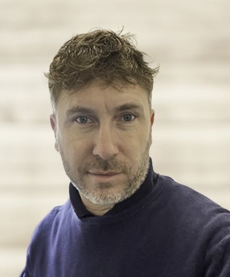 Man with curly hair in blue jumper against striped background