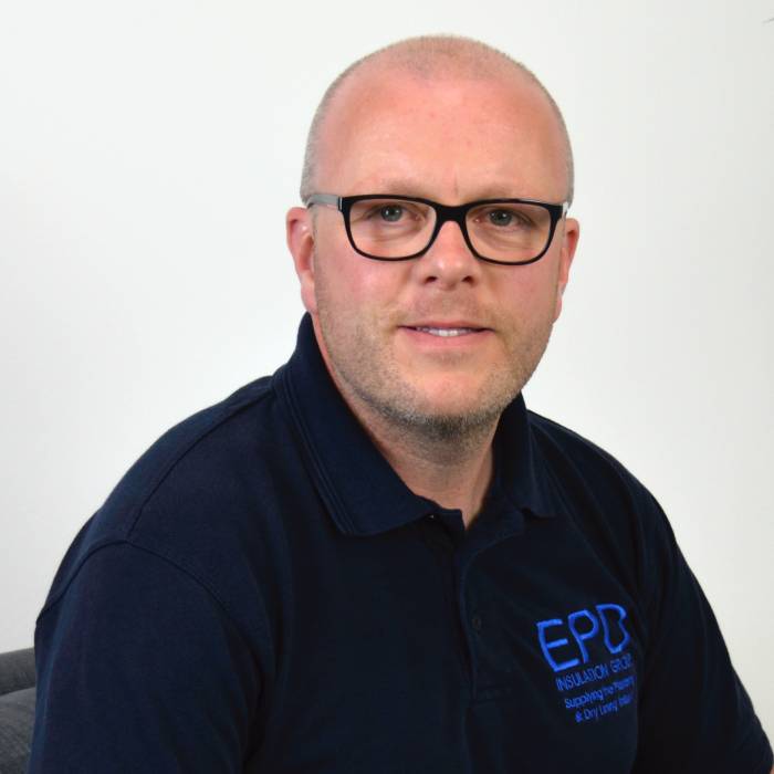 Bald man in glasses wearing navy branded polo shirt.