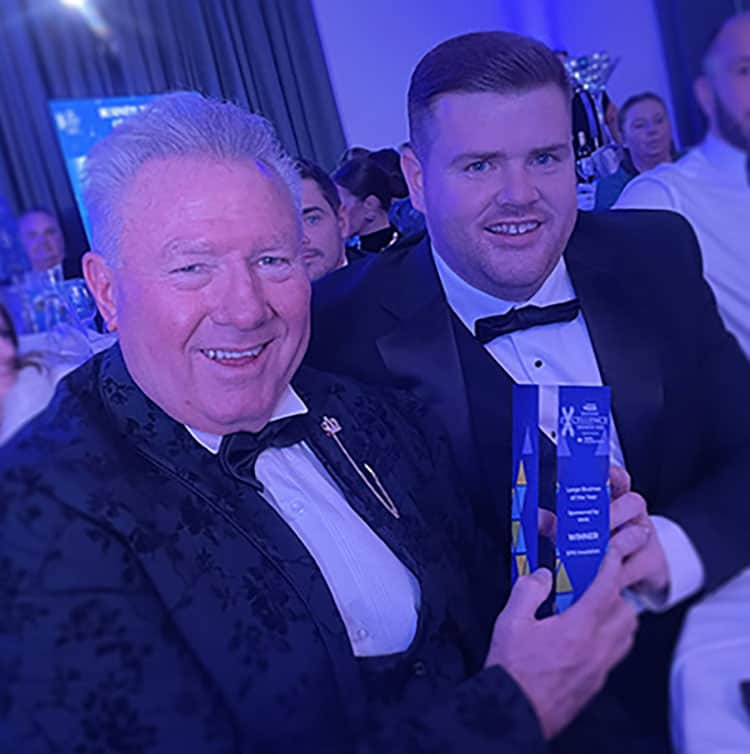 Two men in tuxedos holding award at gala event